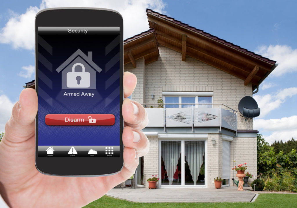 Hand holding app wwith security symbol in front of a home